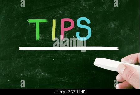 Male hand holding a piece of chalk and "TIPS" note on the blackboard Stock Photo