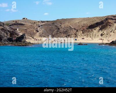 View of a bay with big sandy beach and many bathers between some rocks with deep blue sea on Lanzarote Stock Photo