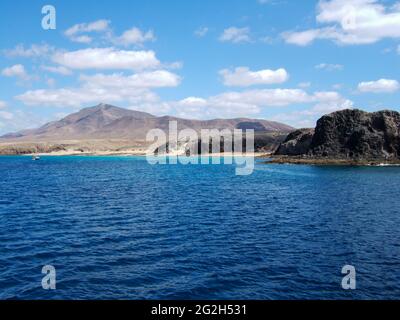 View of a bay with big sandy beach and many bathers between some rocks with deep blue sea on Lanzarote Stock Photo
