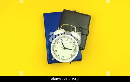 Concept of back to school, students education time background with alarm clock and diary notebooks on the yellow table, top view Stock Photo