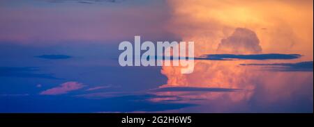 Panorama of the sky with thick clouds formed by the orange sun in the west, purple dark clouds in the evening Stock Photo