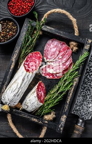 Slices of dry cured salchichon salami in a wooden tray. Black wooden background. Top view Stock Photo