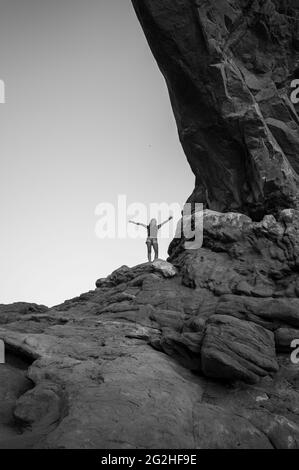 Happy jumping inside the North Window Arch on the north side of the Windows, a sandstone fin featuring 2 massive, eye-shaped openings in Arches National Park, near Moab in Utah, USA. Stock Photo