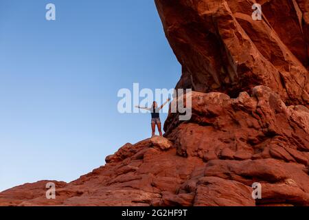 Happy jumping inside the North Window Arch on the north side of the Windows, a sandstone fin featuring 2 massive, eye-shaped openings in Arches National Park, near Moab in Utah, USA. Stock Photo