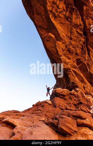 Happy jumping inside the North Window Arch on the north side of the Windows, a sandstone fin featuring 2 massive, eye-shaped openings in Arches National Park, near Moab in Utah, USA. Stock Photo