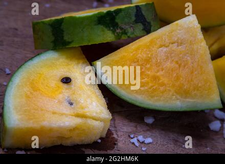 Fresh juicy yellow watermelon cut into triangles on old wooden background. Tropical fruits, Select focus. Stock Photo