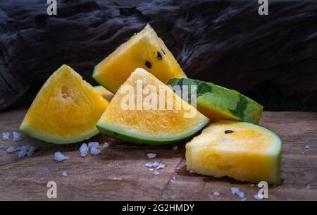 Fresh juicy yellow watermelon cut into triangles on old wooden background. Tropical fruits, Select focus. Stock Photo