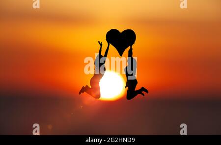 Two women jump with a heart in front of the sun disk Stock Photo