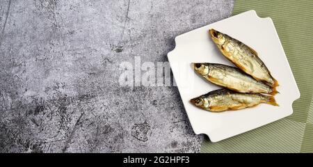 Smoked peled fish (Coregonus peled) on a square plate on a dark background. Top view, flat lay Stock Photo