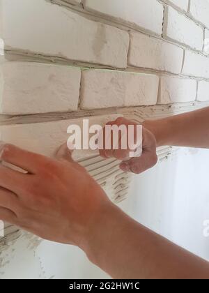 Laying gypsum tiles in rows on the wall with male hands. Home repair. Stock Photo