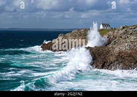 Waves crash on the rocky coast at Pointe du Millier, house and lighthouse Phare du Millier on the cliffs, France, Brittany, Finistère department, Cap Sizun Stock Photo