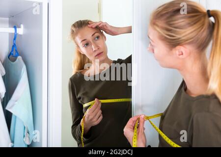 Smiling girl measuring bust with tape measure at home Stock Photo