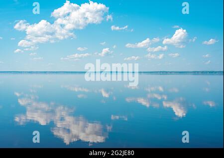 cloudscape. clouds in blue sky and reflection in a large lake. White cumulus clouds in sky over blue sea water. mirror reflection of clouds in lake wa Stock Photo