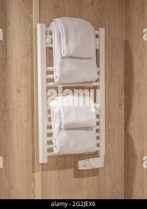 Empty bathroom with gray colored shower wall behind white metal warming rack with white towel folded on top. White towel on a radiator in a bathroom Stock Photo