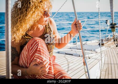 Portrait of attractive middle age woman sitting on the wooden deck of the yacth enjoying the trip - concept of luxury lifestyle with yacht - female people summer day tourist Stock Photo
