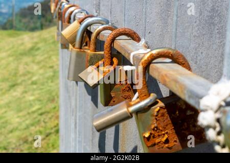 Old rusty love padlocks hanging on railing outdoors. Close up Stock Photo