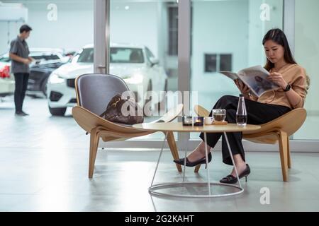 Asian customer woman reading and waiting mechanic checking for maintain her car in maintainance service center with the part of showroom Stock Photo