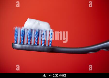 toothbrush with blue bristles and toothpaste on a red background. Stock Photo