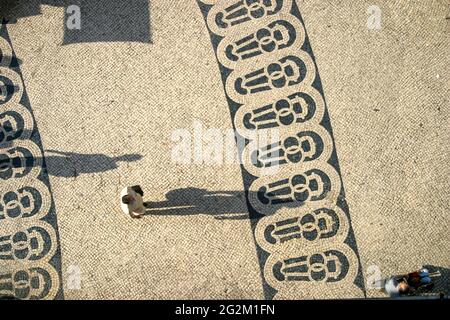 Long shadows of people on a square with pattern of paving stones in Lisbon photographed from above Stock Photo