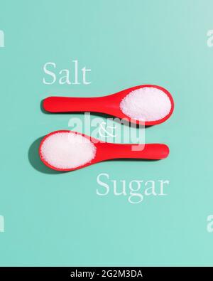Minimalist, contrast, food composition with sea salt and sugar in red plastic spoons and inscription sugar and salt on light blue background Stock Photo