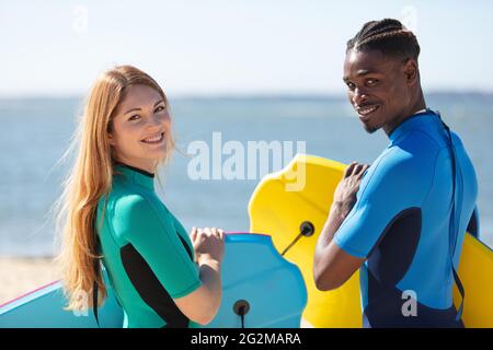 multiracial couple on the beach holding bodyboards Stock Photo