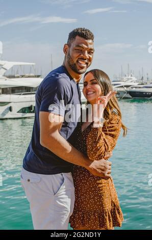Happy multiethnic interracial couple cuddling and smiling while looking at the camera Stock Photo