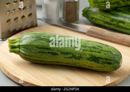 Single fresh raw green spotted courgette on a cuttingboard close up Stock Photo