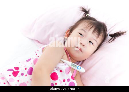 Little asian (thai) girl lying on sickbed with digital thermometer in her armpit, child with fever digital meter show 38.2 celsius is high temperature Stock Photo