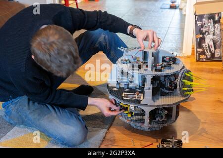 A man in his 30s building a Lego model of the Star Wars Death Star in his living room at home. UK. Theme: adult hobbies, lockdown pass times Stock Photo