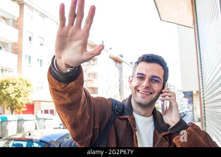 young man waving smiling talking on the phone in the street Stock Photo