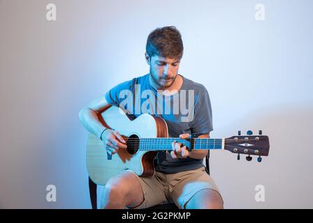 A guitarist plays the guitar sitting on a chair. Studio photo with person isolated on white background. Stock Photo