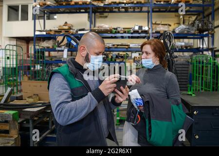 Industrial workers with face masks protected against corona virus discussing about production in factory. People working during COVID-19 pandemic. Stock Photo