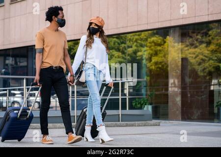 Tourist couple carrying suitcase while walking outdoors. Stock Photo