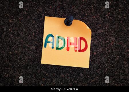 ADHD. The abbreviation ADHD written on a yellow paper note pinned to a cork board. Close up. ADHD is Attention deficit hyperactivity disorder. Stock Photo