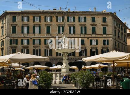Piazza Colombo with the ancient fountain (1646) in its centre and outdoor cafes under sunshades, Genoa, Liguria, Italy Stock Photo