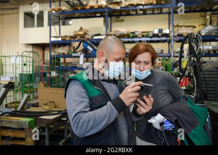 Industrial workers with face masks protected against corona virus discussing about production in factory. People working during COVID-19 pandemic. Stock Photo