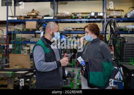 Industrial workers with face masks protected against corona virus discussing about production in factory. People working during COVID-19 pandemic. Stock Photo