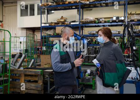 Industrial workers with face masks protected against corona virus discussing about production in factory. People working during COVID-19 pandemic. Stock Photo