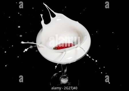 Fresh strawberry falling into glass of milk with a splash Stock Photo