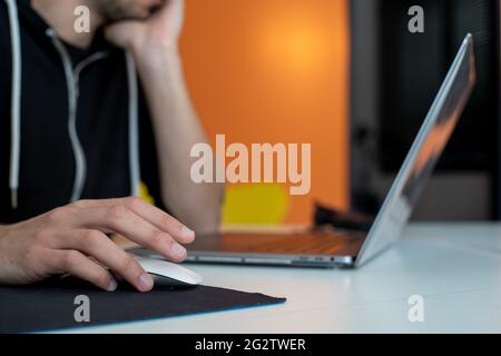 A closeup of a guy's hand clicking a wireless mouse while working on his laptop in his house Stock Photo