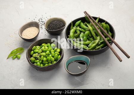 Raw edamame soya beans with salt and sauce on light gray background. Stock Photo