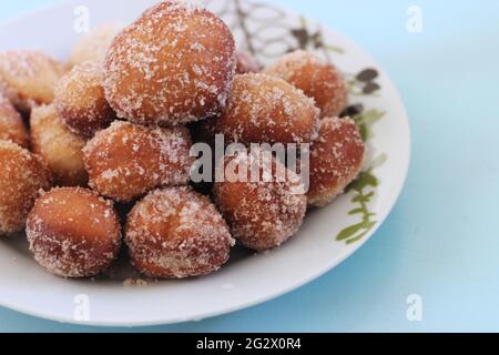 Freshly baked cinnamon sugar doughnuts (Donuts) covered in sugar piled high on top of a floral plate on a teal or light blue background. Stock Photo