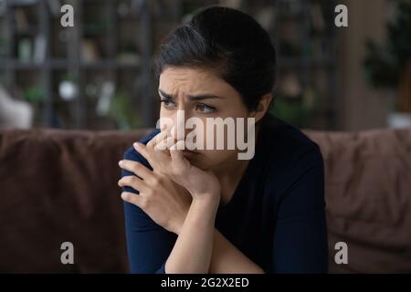 Confused young indian woman sit on couch with sad look Stock Photo