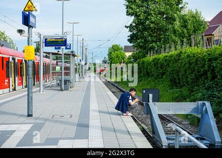 A man crouching on the platform of Altomünster station is busy with his smartphone. Stock Photo