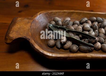 Raw in shell whole Pecan nuts in a wooden bowl on a wood table with a vintage nut cracker Stock Photo