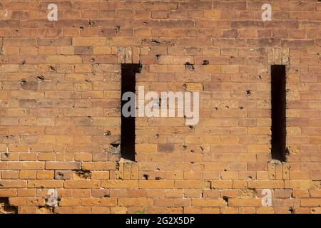 A loophole in an old stone wall. The fortification stone wall of an ancient castle with loopholes. Bullet and cannonball marks on the wall. Textured b Stock Photo