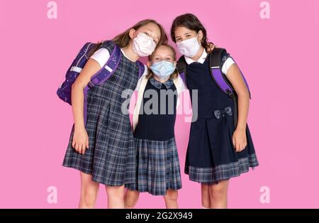 Three happy girls with long hair in school uniforms wearing medical masks. STop coronavirus. Distance learning. Studio photo. Back to school. Stock Photo