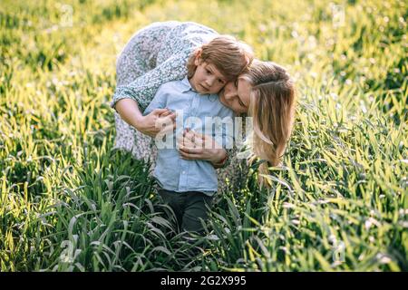 Mom gently hugs her son 3 years old, they walk outdoors in field on summer day Stock Photo