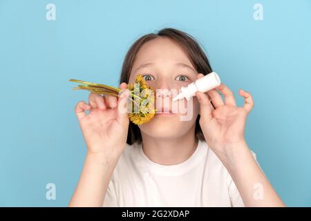 Portrait of a child girl with flowers in her teeth and anti-allergic pills and spray in her hands on a blue background. The concept of seasonal pollen Stock Photo