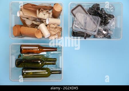 Sorting garbage. Three transparent containers with trash on a blue background: glass, plastic, paper. Stock Photo